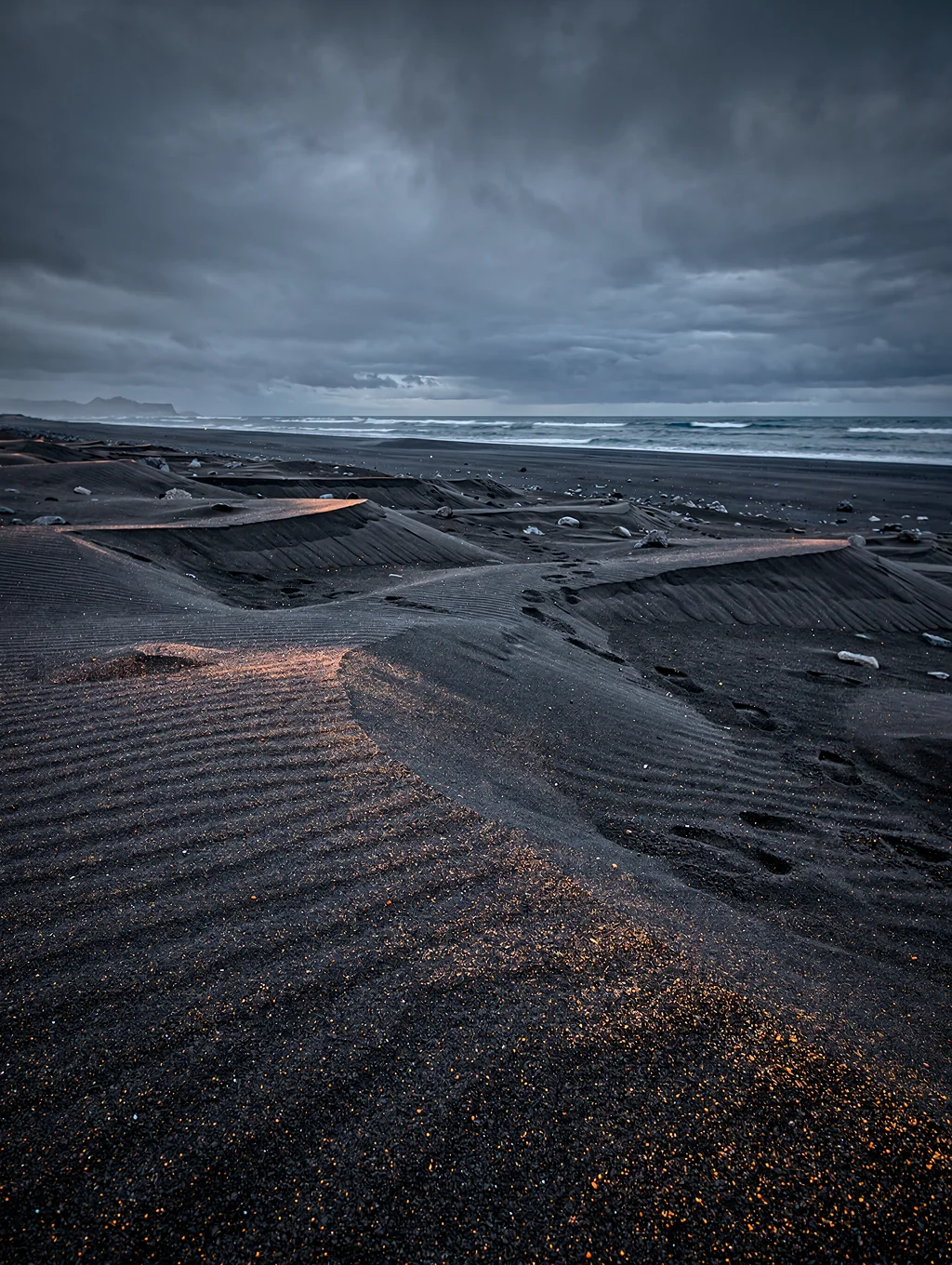 Black volcanic sand with crystalline ice fragments at dusk